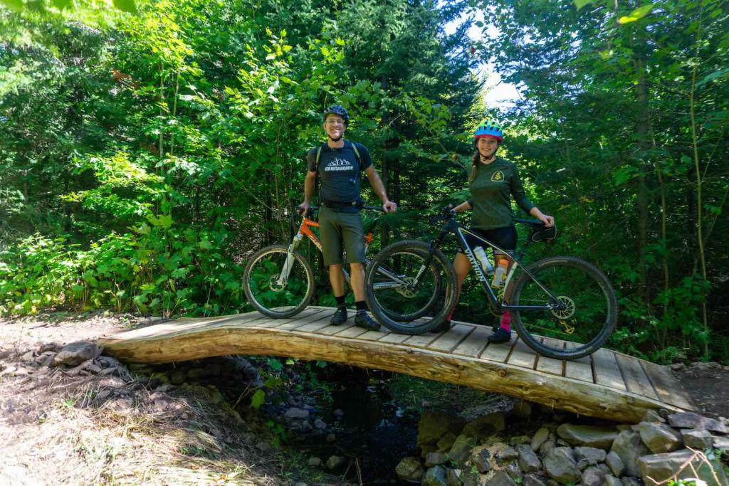 A father daughter duo poses with their mountain bikes on a bridge.